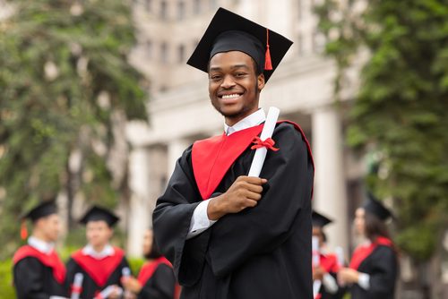 Cheerful,African,American,Guy,In,Graduation,Costume,Showing,His,Diploma